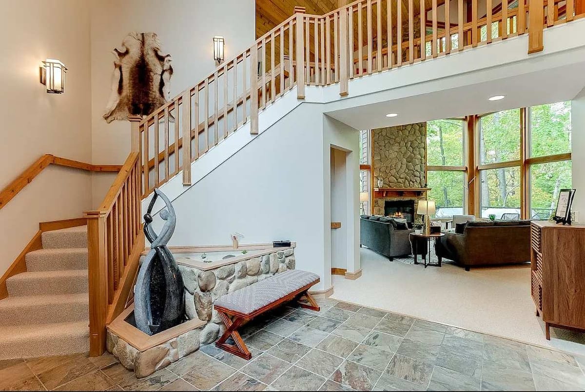 Grand entryway with staircase, loft railing, and great room with stone fireplace beyond